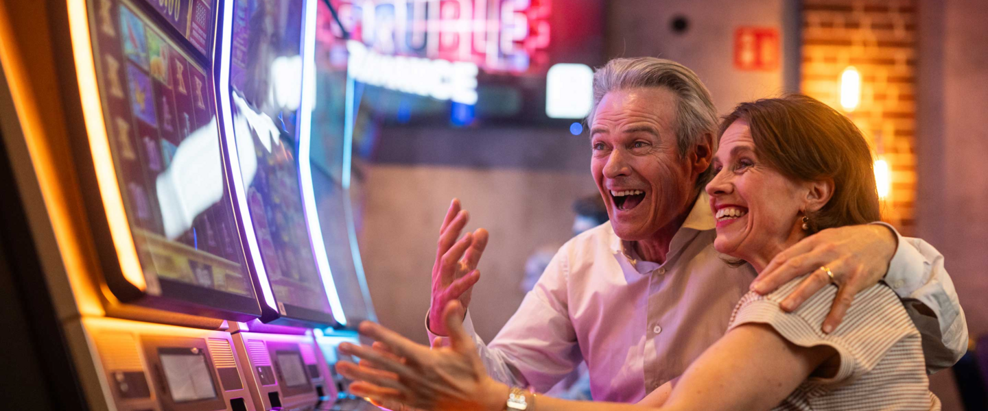 Ein Mann hält eine Frau im Arm und beide freuen sich über einen Gewinn an einem Spielautomaten.